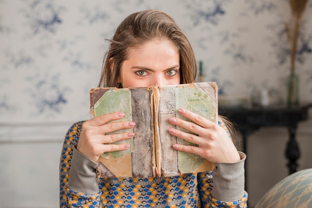 Junge Frau, die ihren Mund mit heftigem verwittertem Buch bedeckt