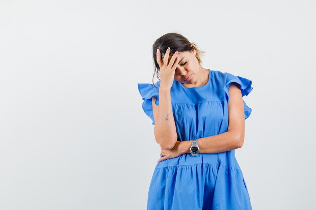 Junge Frau, die im blauen Kleid die Hand auf die Stirn hält und erschöpft aussieht