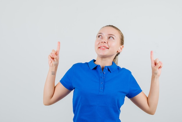 Junge Frau, die im blauen T-Shirt oben zeigt und fröhlich schaut