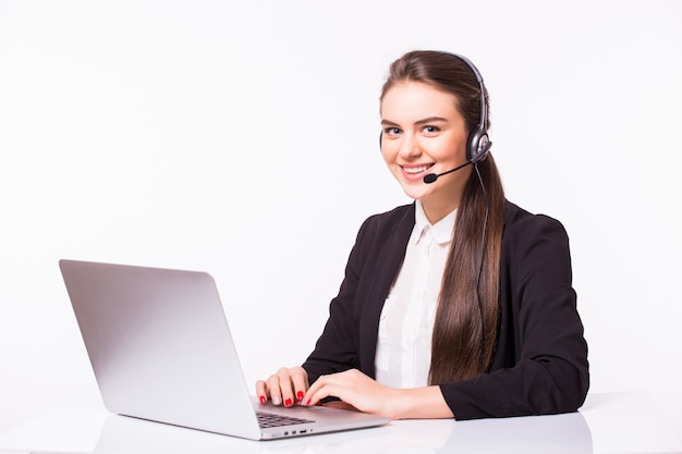 Junge Frau, die im Büro mit Laptop und Kopfhörern auf weißer Wand, Kundendienst und Callcenter arbeitet.