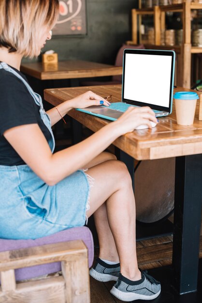 Junge Frau, die im Café unter Verwendung des tragbaren Laptops sitzt