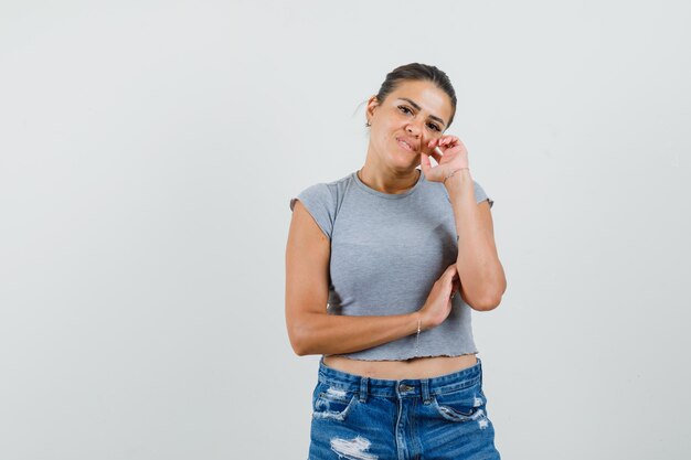 Junge Frau, die im Denken steht, posiert im T-Shirt, in den Shorts und sieht vernünftig aus.