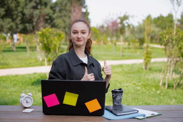 Junge Frau, die im Freien am Laptop arbeitet und super lächelnd zeigt