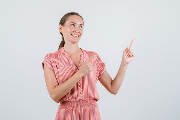 Junge Frau, die im gestreiften Kleid zeigt und fröhlich aussieht. Vorderansicht.