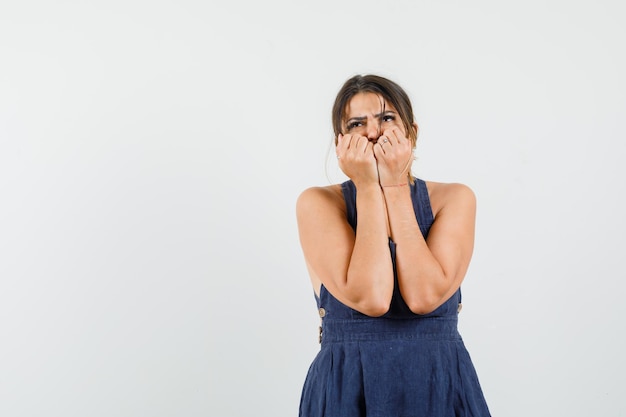 Junge Frau, die im Kleid die Fäuste im Gesicht hält und verängstigt aussieht