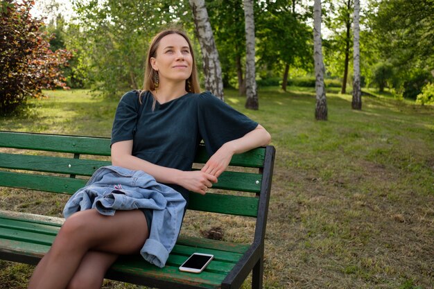 Junge Frau, die im Park sitzt, der auf einem Stuhl sitzt