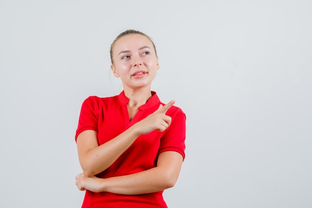 Junge Frau, die im roten T-Shirt weg zeigt und hoffnungsvoll aussieht