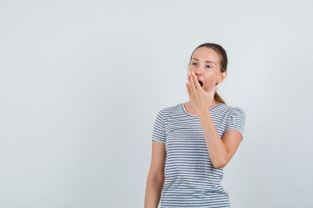 Junge Frau, die im T-Shirt gähnt und schläfrig aussieht. Vorderansicht.