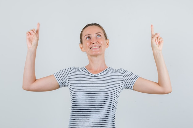 Junge Frau, die im T-Shirt zeigt und hoffnungsvoll aussieht. Vorderansicht.