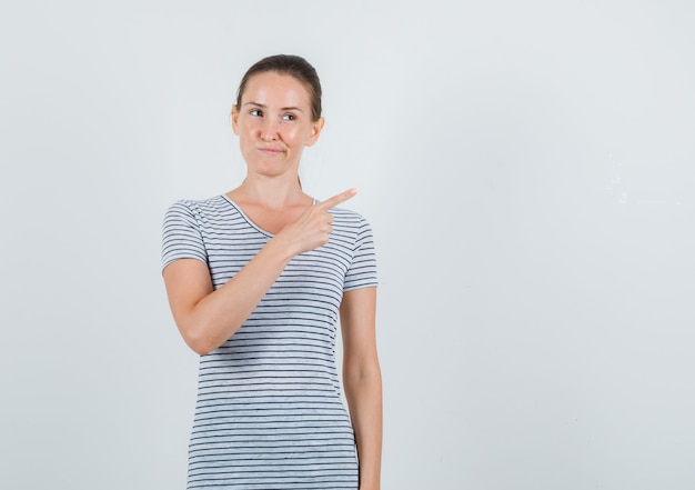 Junge Frau, die im T-Shirt zur Seite zeigt und neugierig schaut, Vorderansicht.