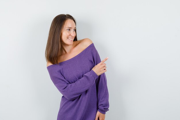 Junge Frau, die im violetten Hemd zur Seite zeigt und freudige Vorderansicht schaut.