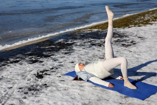 Kostenloses Foto junge frau, die im winter am strand yoga im freien praktiziert