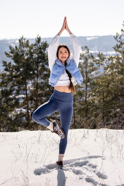 Kostenloses Foto junge frau, die im winter yoga im freien praktiziert, umgeben von bäumen