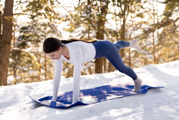 Kostenloses Foto junge frau, die im winter yoga im freien praktiziert, umgeben von bäumen