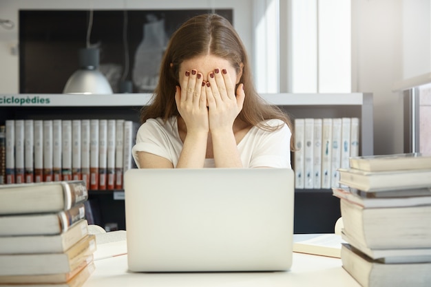 Junge Frau, die in Bibliothek mit Laptop sitzt