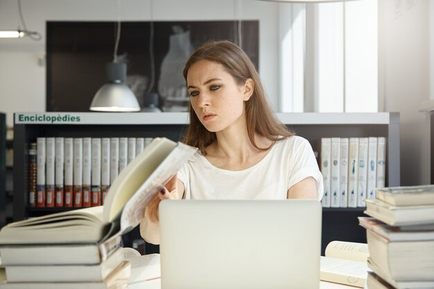 Junge Frau, die in Bibliothek mit Laptop sitzt