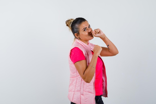 Junge Frau, die in Boxerpose in rosa T-Shirt und Jacke steht und glücklich aussieht looking