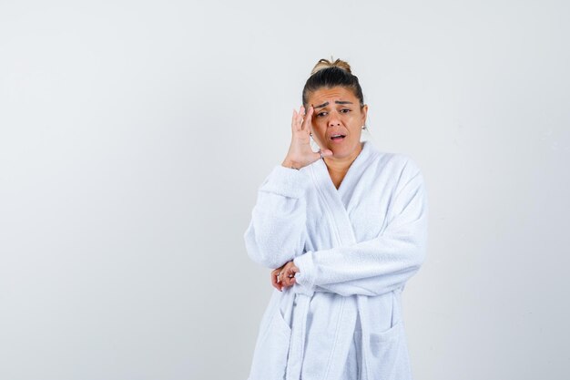 Junge Frau, die in denkender Pose im Bademantel steht und vergesslich aussieht