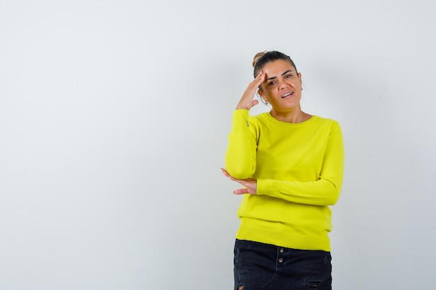 Junge Frau, die in denkender Pose in Pullover, Jeansrock steht und nachdenklich aussieht