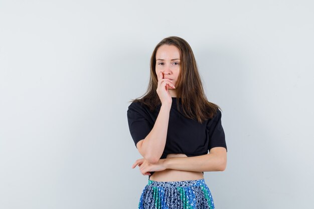 Junge Frau, die in der denkenden Haltung steht und in schwarzem T-Shirt und blauem Rock wegschaut und nachdenklich schaut