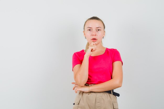 Junge Frau, die in der denkenden Pose im T-Shirt und in der Hose steht und vernünftig aussieht