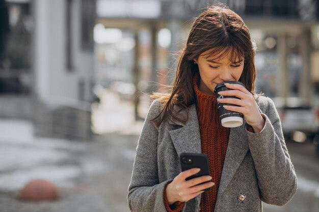 Junge Frau, die in der Straße geht und Kaffee trinkt