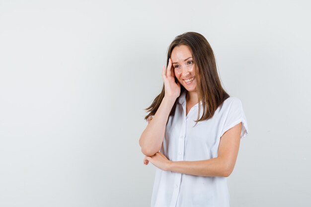 Junge Frau, die in der weißen Bluse lächelt und optimistisch schaut.