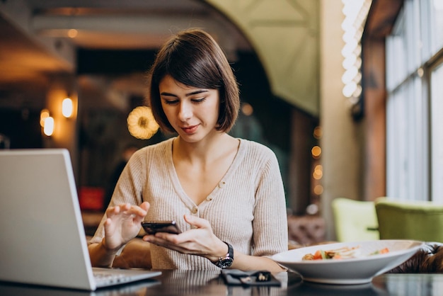 Junge Frau, die in einem Café zu Mittag isst und am Laptop arbeitet