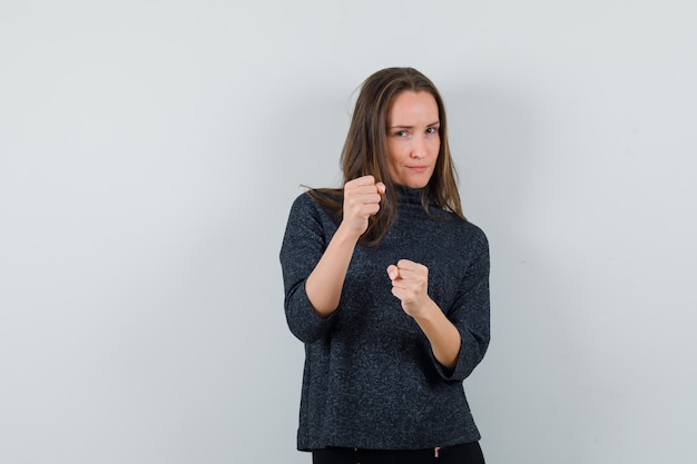 Junge Frau, die in einer Boxerhaltung im Hemd steht und zuversichtlich schaut. Vorderansicht.