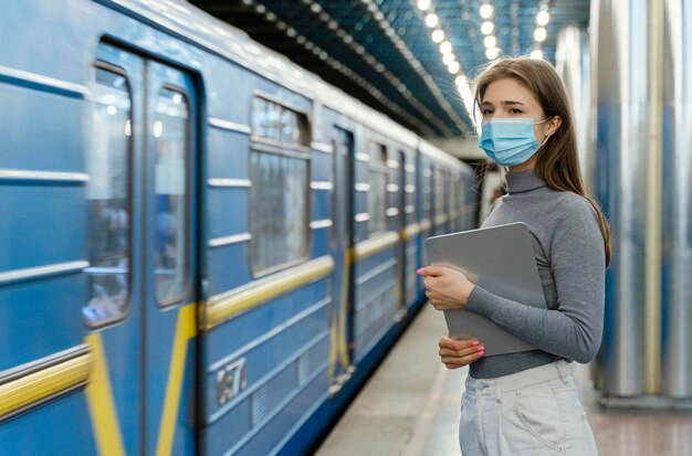 Junge Frau, die in einer U-Bahnstation mit einer Tablette wartet