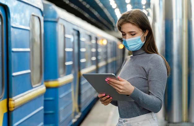 Junge frau, die in einer u-bahnstation mit einer tablette wartet