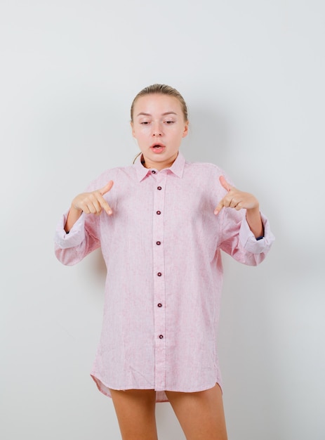 Junge Frau, die in rosa Hemd unten zeigt und ängstlich schaut