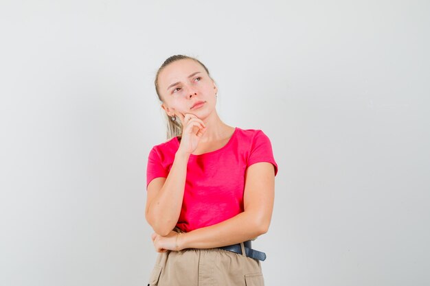 Junge Frau, die in T-Shirt, Hosen und nachdenklich schaut. Vorderansicht.