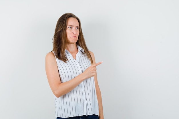 Junge Frau, die in T-Shirt, Jeans zur Seite zeigt und traurig aussieht. Vorderansicht.