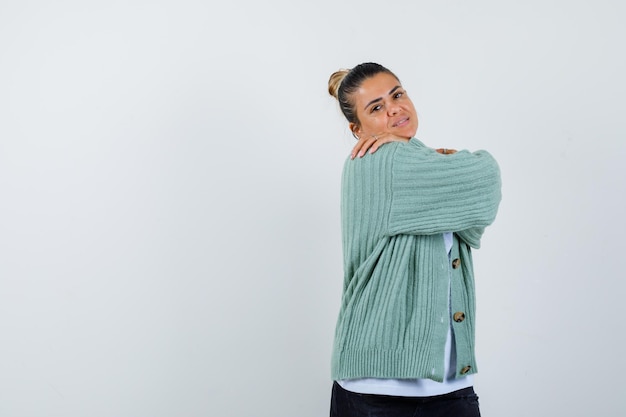 Junge Frau, die in weißem T-Shirt und mintgrüner Strickjacke über die Schulter schaut und attraktiv aussieht