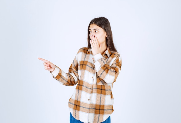 junge Frau, die irgendwo auf der weißen Wand steht und zeigt.