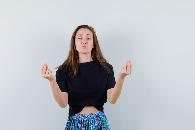 Junge Frau, die italienische Geste im schwarzen T-Shirt und im blauen Rock zeigt und glücklich schaut