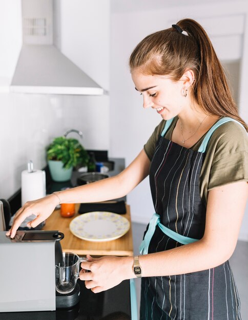 Junge Frau, die Kaffee von der EspressoKaffeemaschine nimmt