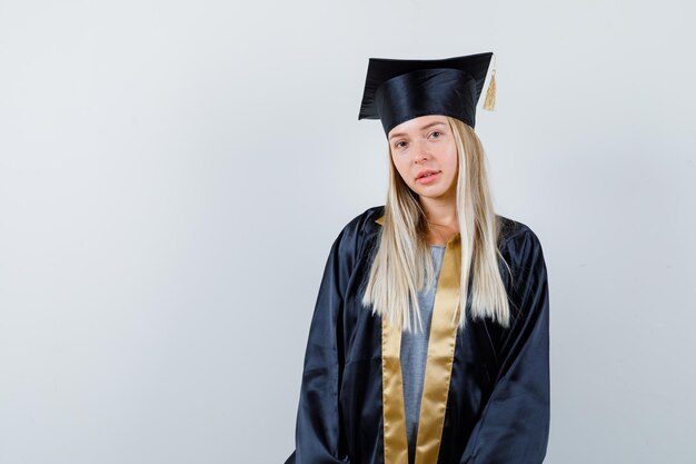 Junge Frau, die Kamera in der Absolventenuniform betrachtet und attraktiv schaut.