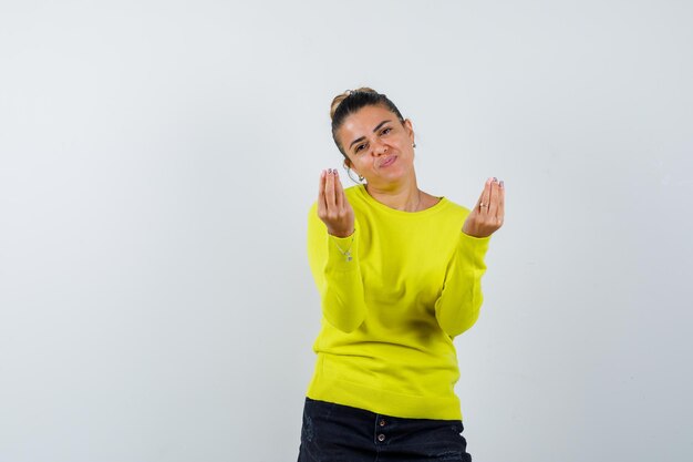 Junge Frau, die köstliche Geste in Pullover, Jeansrock zeigt und erfreut aussieht looking