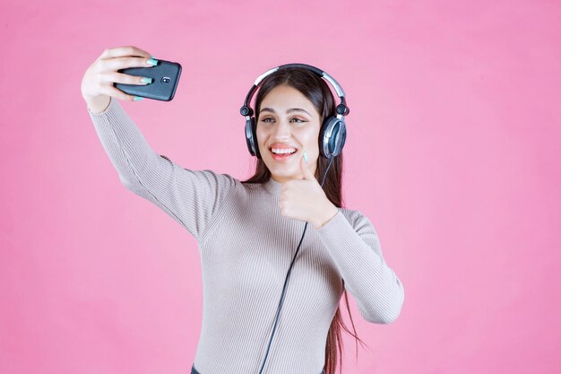 Junge Frau, die Kopfhörer trägt und ihr Selfie nimmt