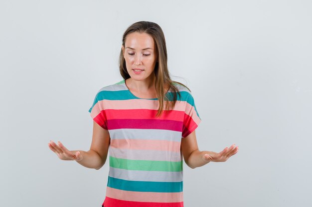 Junge Frau, die langsame Geste im T-Shirt zeigt und ruhige Vorderansicht schaut.