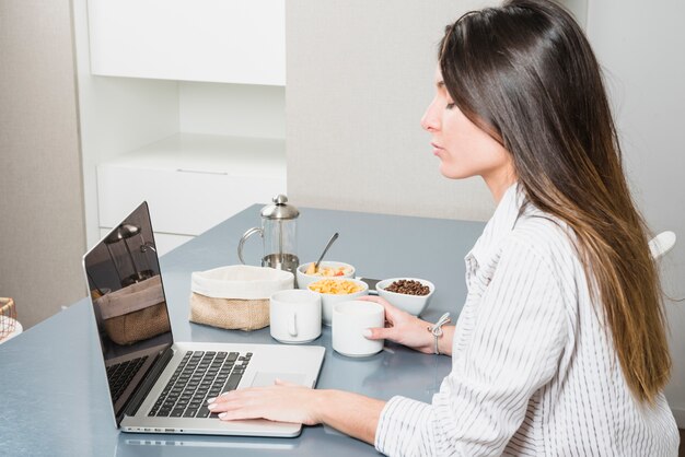 Junge Frau, die Laptop am Frühstückstische verwendet