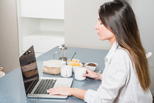 Junge Frau, die Laptop am Frühstückstische verwendet