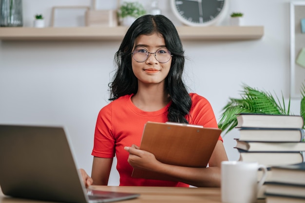 Junge Frau, die Laptop auf Schreibtisch benutzt und Akten hält