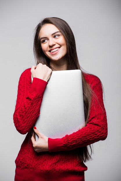 Junge Frau, die Laptop hält und hält. Glückliches junges Mädchen, das ihren Laptop benutzt, lokalisiert auf weißer Wand.