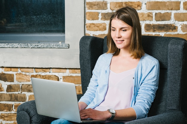 Kostenloses Foto junge frau, die laptop im lehnsessel verwendet