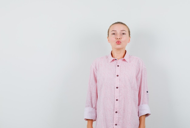 Junge Frau, die Lippen im rosa Hemd gefaltet hält und hübsch aussieht