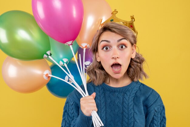 junge Frau, die Luftballons in der Krone auf Gelb hält