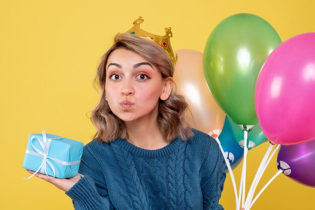 junge Frau, die Luftballons und wenig Geschenk auf Gelb hält